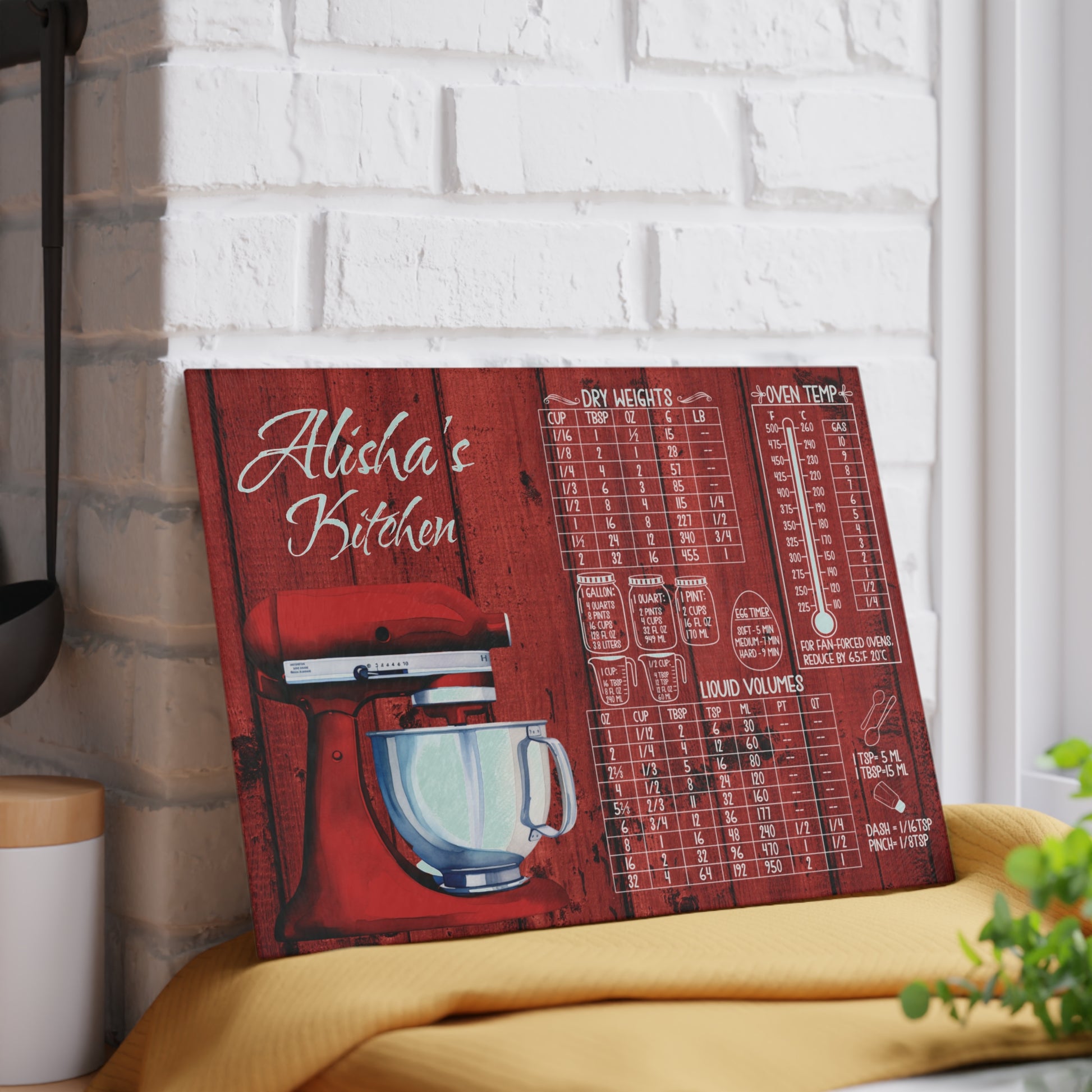 Personalized glass cutting board featuring a red stand mixer illustration, kitchen measurement and oven temperature conversion charts, and custom name displayed on a kitchen counter.