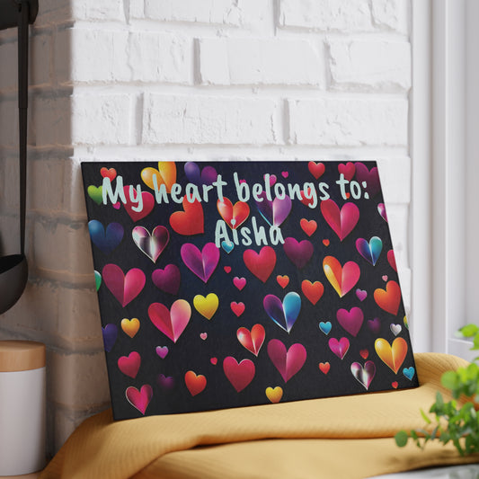 Personalized glass cutting board featuring colorful heart patterns on a black background with custom name text displayed on a kitchen counter.